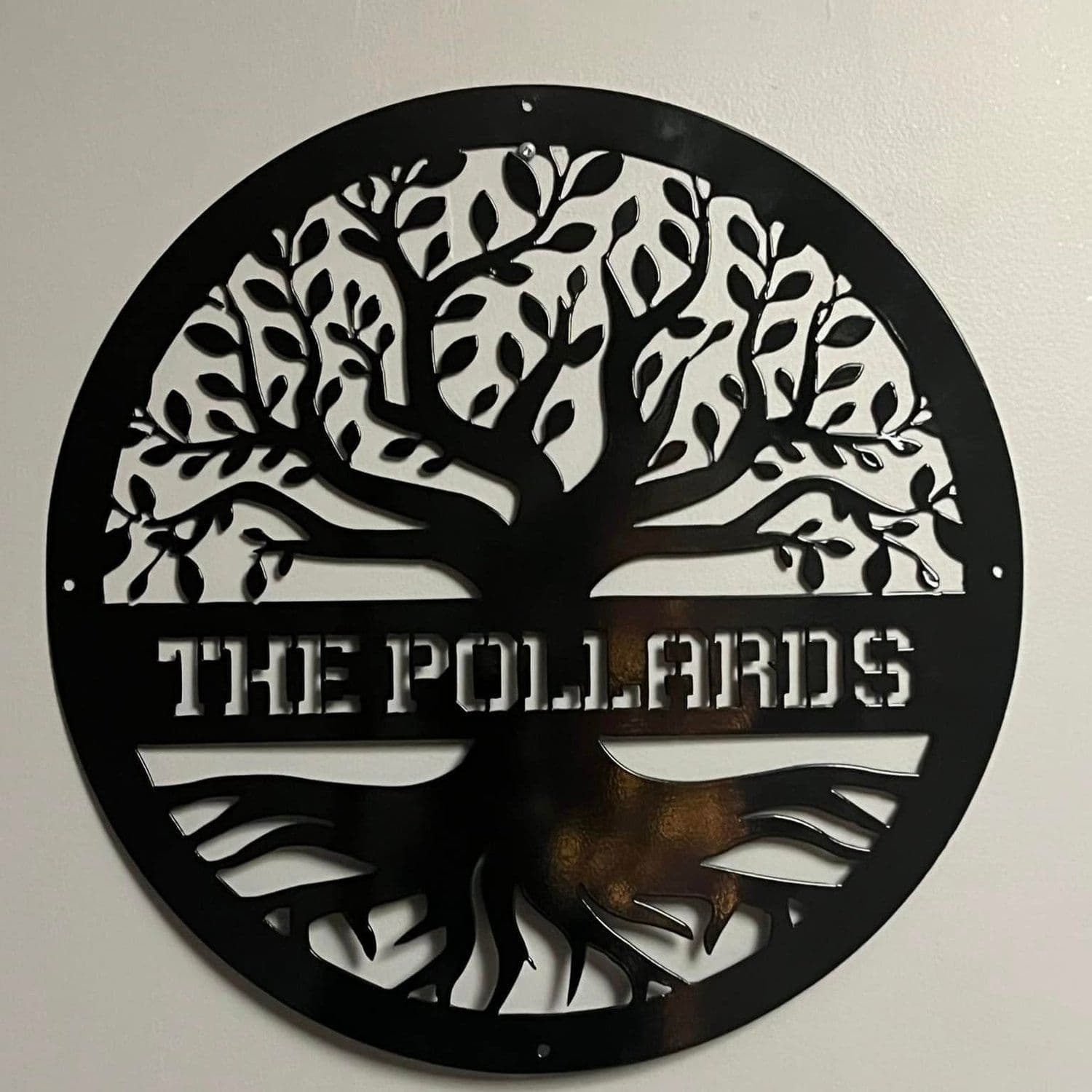 A round black plasma-cut steel sign with a tree and the words The Pollards